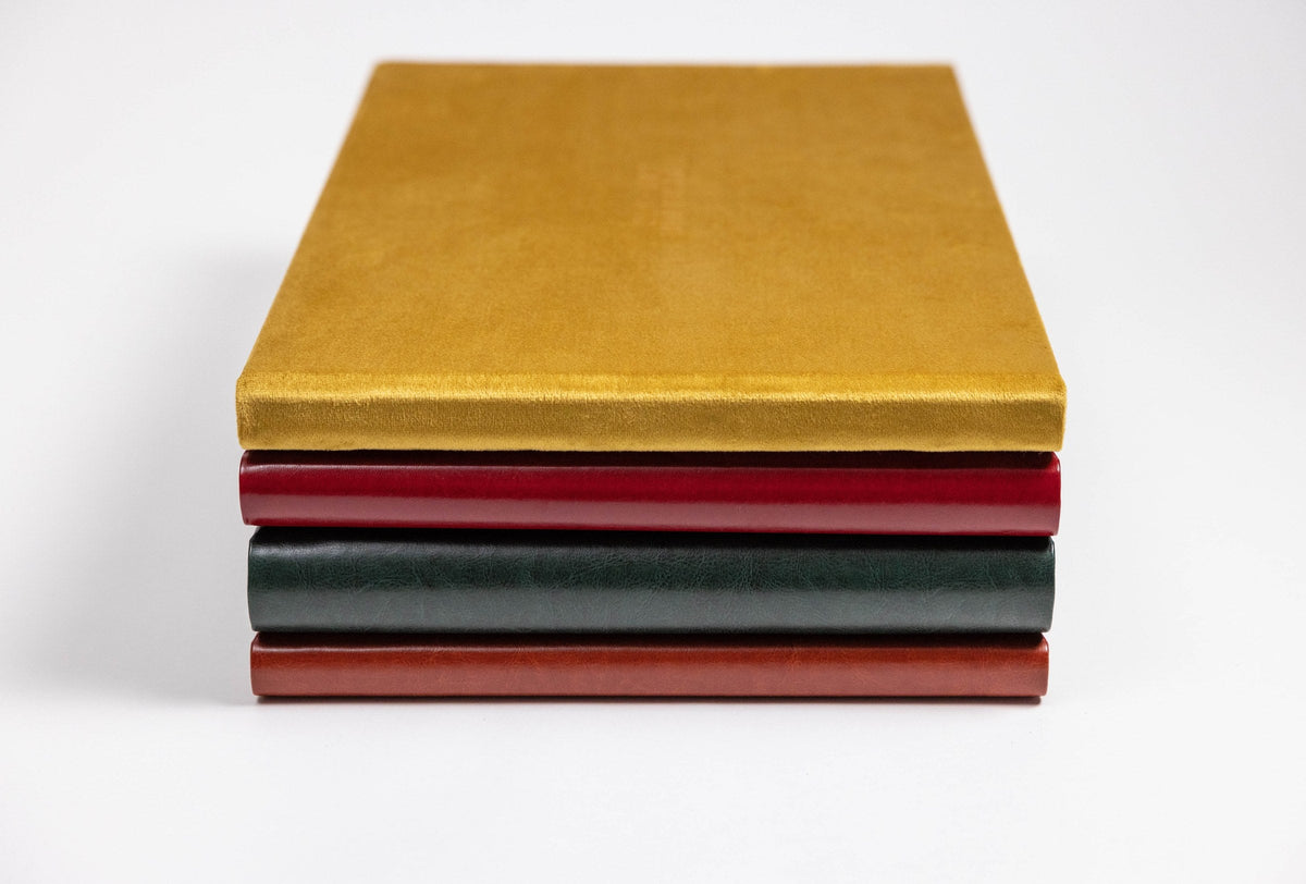Stack of velvet and leatherette wedding albums in mustard, red, green and brown