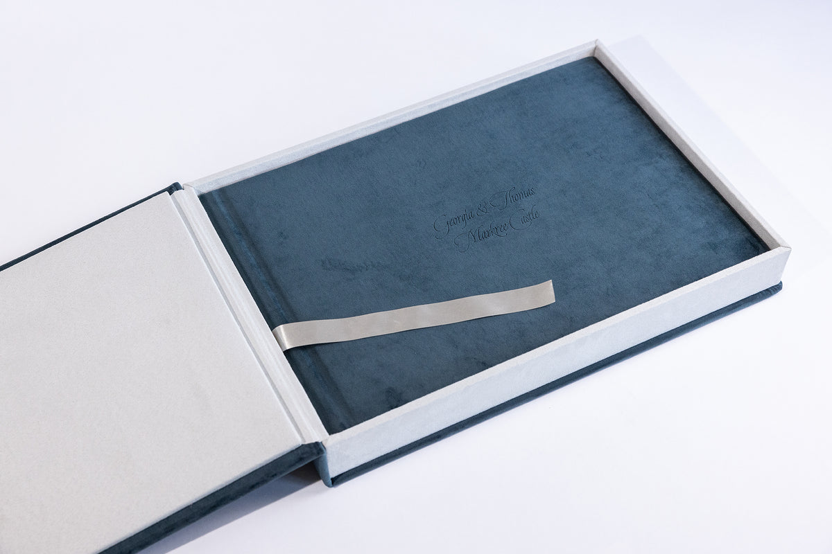 Deep Sea Blue velvet wedding album with engraved cover text, inside its open matching album box