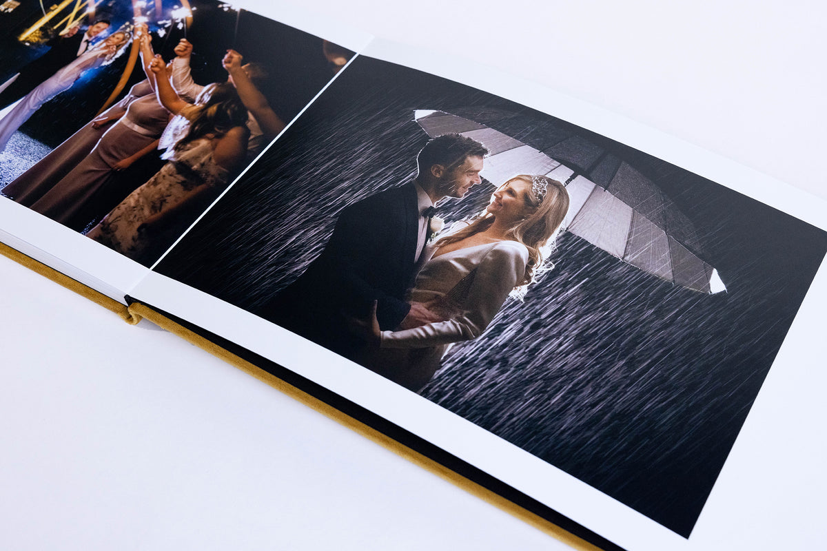 Open Dijon Yellow velvet wedding album showing lay-flat pages with a couple under an umbrella in the rain