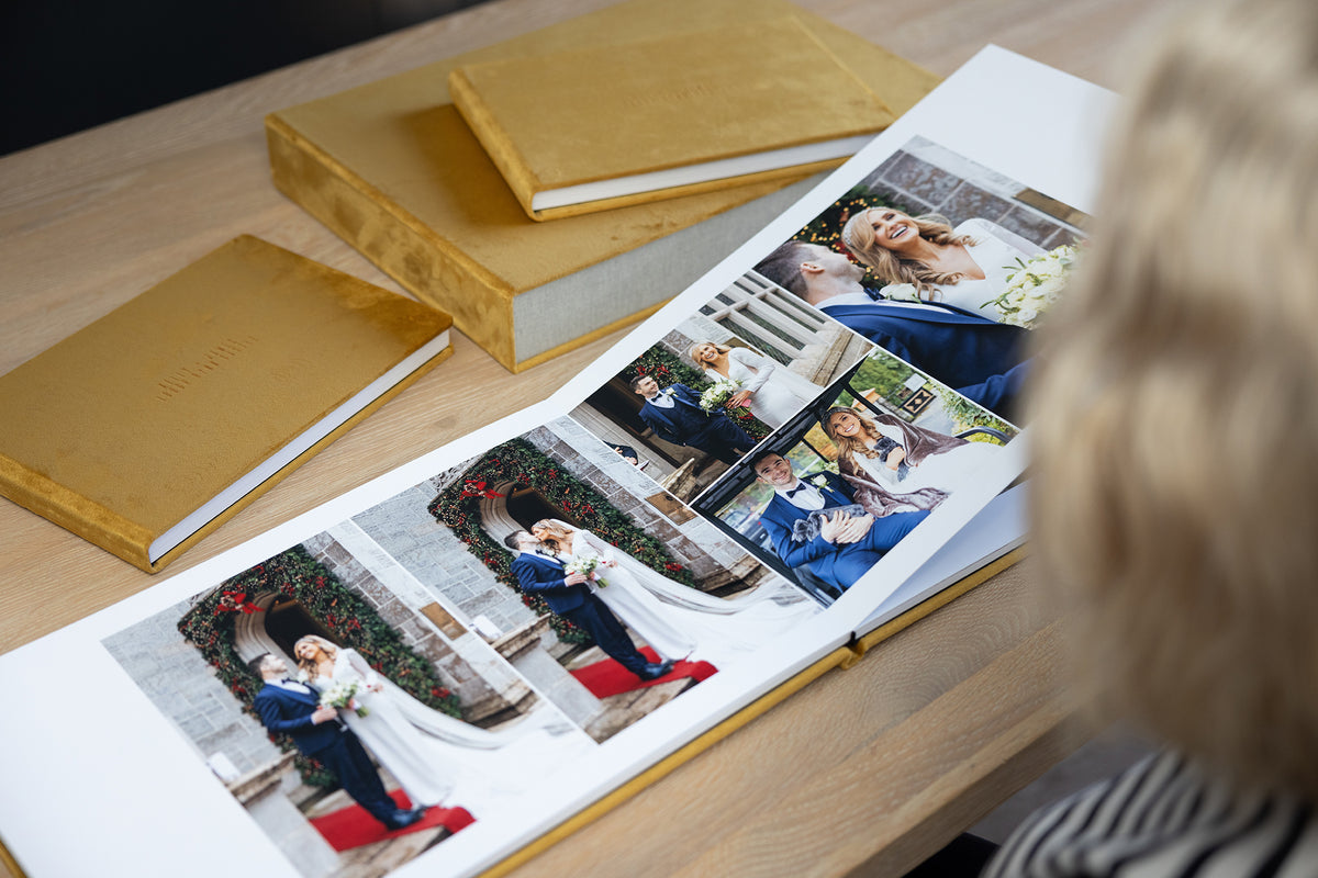 Woman looking through an open Dijon Yellow velvet wedding album, with matching parent albums and album box on the table