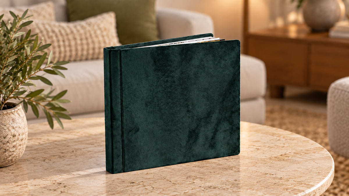Handcrafted emerald green velvet square wedding album standing on a marble coffee table in a softly lit living room