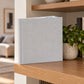 Mist Grey linen wedding album standing on a wooden shelf in a bright living room
