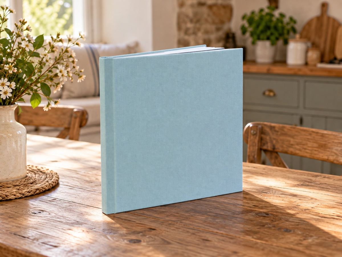 Pigeon Blue linen wedding album standing on a rustic wooden table in a sunlit kitchen